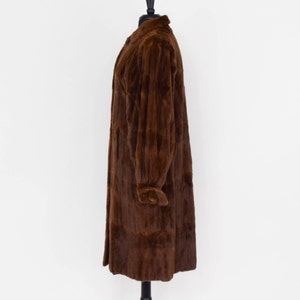 May include: A long brown fur coat with a collar and long sleeves. The coat is on a mannequin and is displayed against a white background.