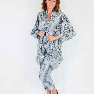 May include: A woman wearing a gray and black snake print jumpsuit with a long-sleeved top and pants. She is wearing silver sneakers.