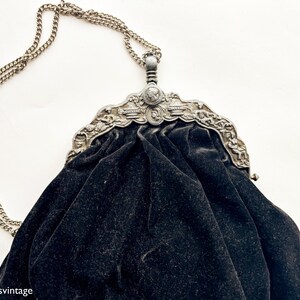 May include: A vintage black velvet evening bag with a silver chain and ornate metal clasp. The clasp features a detailed design with a central medallion.
