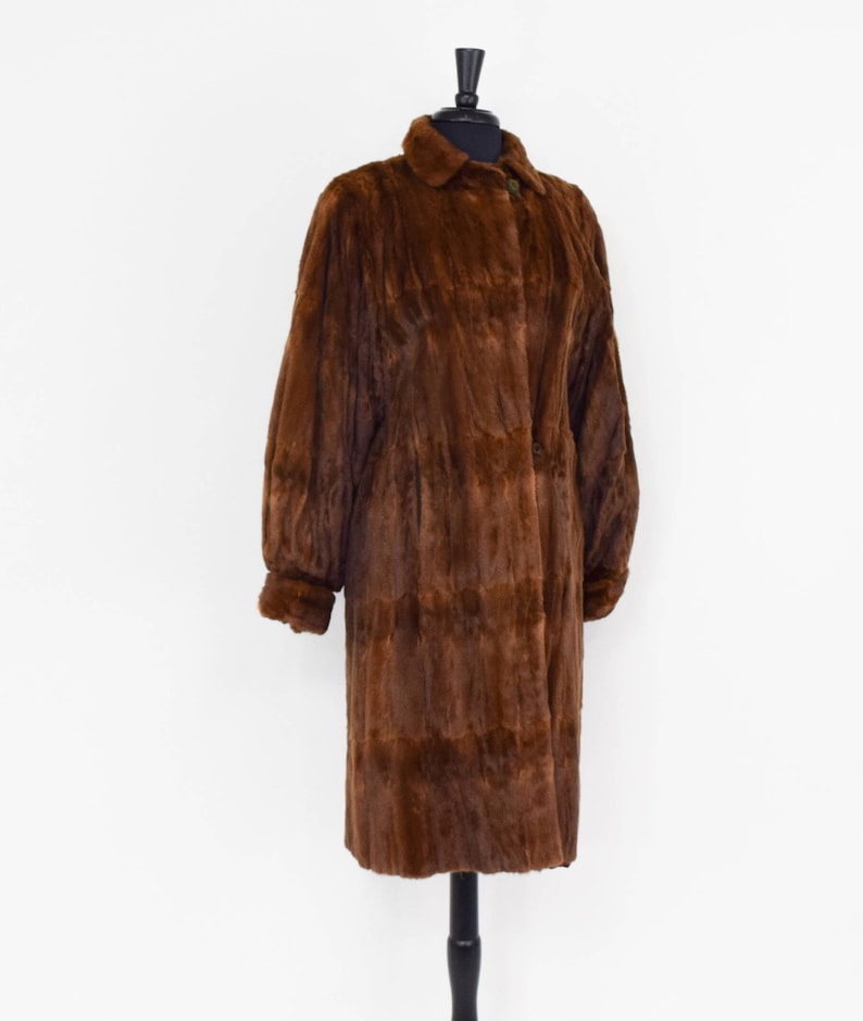May include: A long brown fur coat with a collar and button closure.