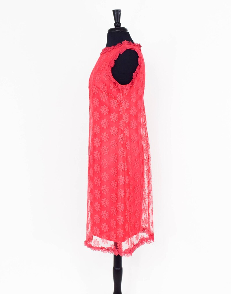 May include: A coral pink sleeveless dress with a floral pattern and lace trim. The dress is on a mannequin.
