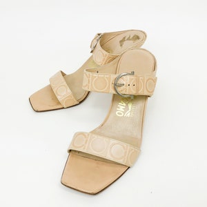 May include: A pair of beige leather heeled sandals with a buckle closure and the brand name "Salvatore Ferragamo" printed on the straps.