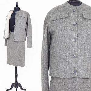May include: A gray tweed skirt suit with a button-up jacket and a matching skirt. The jacket has two flap pockets on the front and the skirt is knee-length.