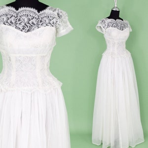 Puede incluir: Un vestido de novia blanco de encaje con un corpi&ntilde;o ajustado y una falda completa. El vestido tiene un escote de coraz&oacute;n y mangas cortas.