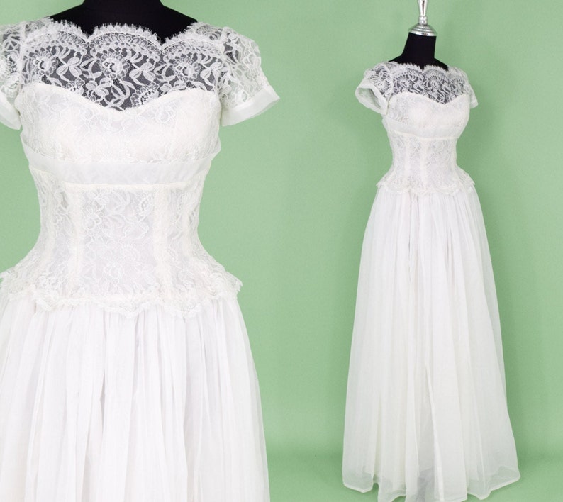 Puede incluir: Un vestido de novia blanco de encaje con un corpi&ntilde;o ajustado y una falda completa. El vestido tiene un escote de coraz&oacute;n y mangas cortas.