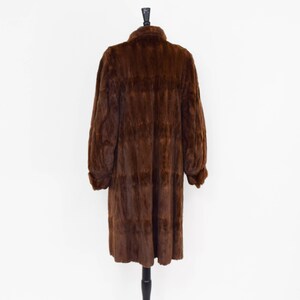May include: A long brown fur coat with a collar and long sleeves. The coat is hanging on a mannequin.