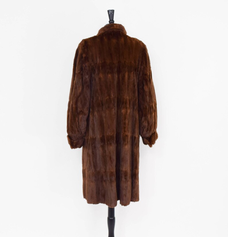 May include: A long brown fur coat with a collar and long sleeves. The coat is hanging on a mannequin.