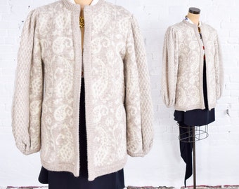 Puede incluir: Un cárdigan de color crema con un estampado paisley blanco. El cárdigan tiene manga larga y un corte holgado.