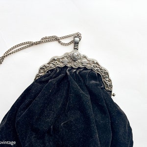 May include: A black velvet evening bag with a silver ornate metal frame and a chain strap.