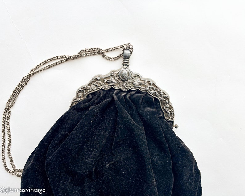 May include: A black velvet evening bag with a silver ornate metal frame and a chain strap.