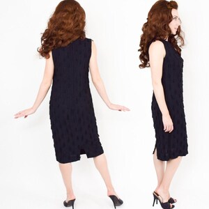 May include: A black sleeveless dress with a textured, raised pattern. The dress has a fitted silhouette and a knee-length hemline. The dress has a slit on the back.