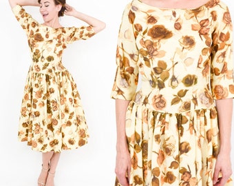 May include: A vintage floral dress with a fitted bodice and a full skirt. The dress is made of a light yellow fabric with a brown and white floral print. The dress has a boat neck and three-quarter sleeves.