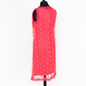 May include: A coral pink sleeveless dress with a floral lace pattern. The dress has a scalloped hemline and is displayed on a mannequin.