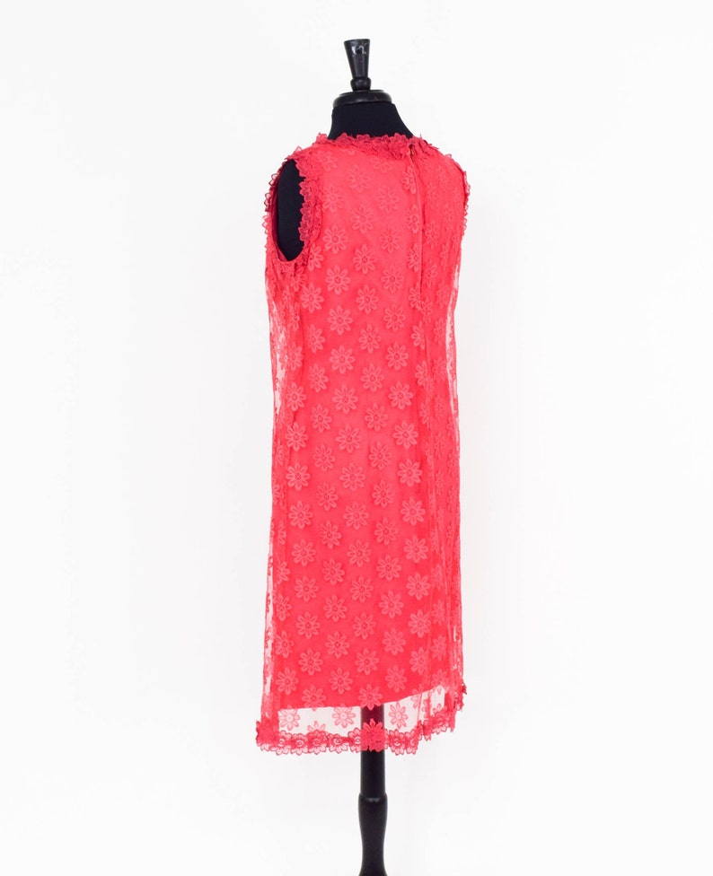May include: A coral pink sleeveless dress with a floral lace pattern. The dress has a scalloped hemline and is displayed on a mannequin.