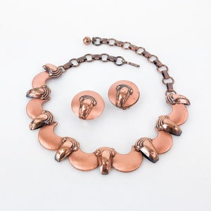 May include: A copper necklace with a chain and matching earrings. The necklace features a series of crescent-shaped pendants with a decorative design.