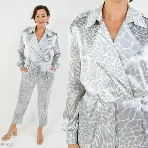 Op de afbeelding: Een zilveren en witte satijnen jumpsuit met dierenprint, een wikkelhalslijn en lange mouwen.