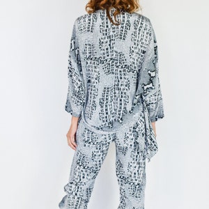 May include: A gray and black patterned pantsuit with a long-sleeved top and cropped pants. The top has a loose fit and a tie at the waist. The pants have a relaxed fit and a cuffed hem.