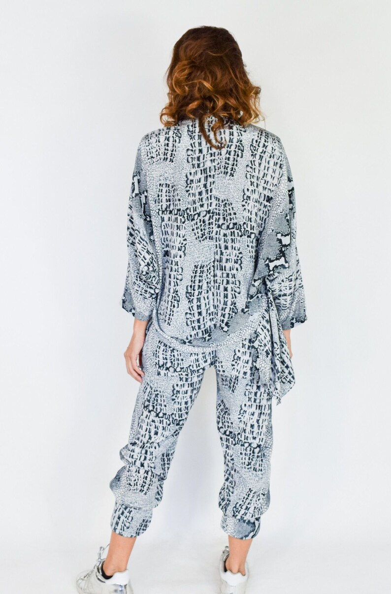 May include: A gray and black patterned pantsuit with a long-sleeved top and cropped pants. The top has a loose fit and a tie at the waist. The pants have a relaxed fit and a cuffed hem.