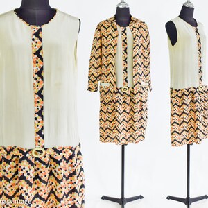 May include: A two-piece vintage dress set with a sleeveless, cream-colored top and a black, orange, and yellow geometric print skirt. The skirt has a gold belt.
