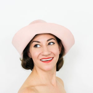 May include: A woman wearing a light pink wide-brimmed hat. She is looking up and smiling.