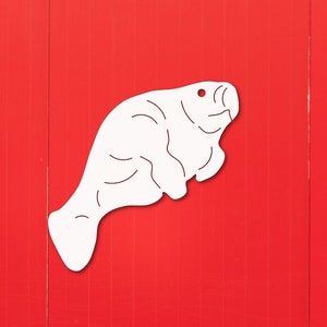 May include: A white silhouette of a manatee is painted on a red wall. The manatee is facing right and has a slightly open mouth.