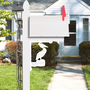 May include: White mailbox with a pelican design mailbox post. The mailbox is mounted on a white post with a black lamp post next to it.