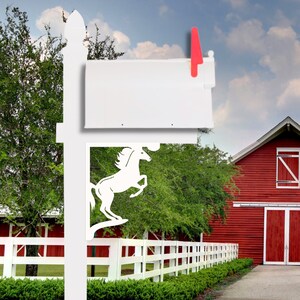 Puede incluir: Buzón de metal blanco con un diseño de silueta de caballo. El buzón está montado en un poste blanco con un granero rojo en el fondo.
