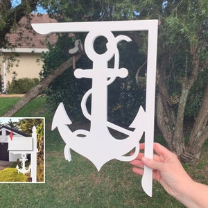Op de afbeelding: Witte brievenbusbeugel in de vorm van een anker. De houten beugel is ontworpen om op een paal te worden gemonteerd. Het ankerontwerp, inclusief een touw, is een decoratief element voor een brievenbus.