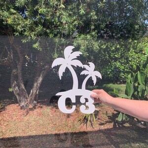 Puede incluir: Calcomanía de vinilo blanco con dos palmeras y el texto "C3" sobre un fondo blanco. La calcomanía se está sujetando contra una ventana.