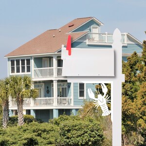 May include: A white mailbox with a lobster design mounted on a wooden post in front of a blue and white house. The mailbox is attached to the post with a red bracket.