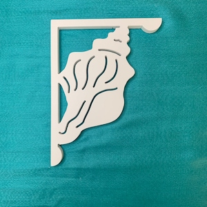 May include: White wooden shelf bracket with a seashell design. The bracket is shaped like a seashell with a detailed design of the shell's ridges and curves.