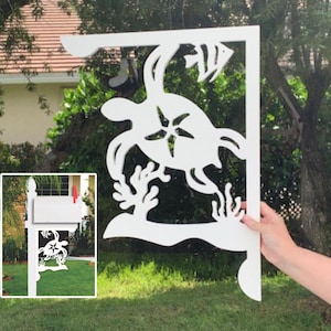 May include: White wooden mailbox bracket with a cutout design of a sea turtle, starfish, and coral. The bracket is mounted on a wooden post and is holding a white mailbox.