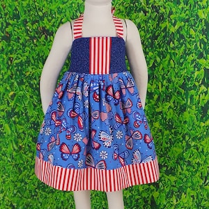 May include: A blue and red sleeveless dress with a red, white, and blue striped bodice and a skirt featuring a butterfly pattern with red, white, and blue accents.