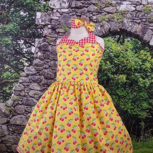 May include: A yellow dress with a cherry print and red and white gingham trim. The dress has a halter neckline and a full skirt. It comes with a matching red and white gingham headband.