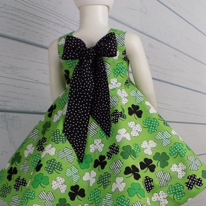May include: A green dress with a shamrock print and a black polka dot bow in the back. The dress has a full skirt and is perfect for St. Patrick's Day.