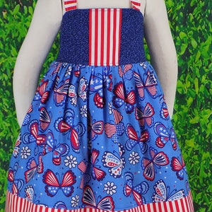 May include: A blue and red sleeveless dress with a butterfly print. The dress has a red, white, and blue striped bodice and hem.