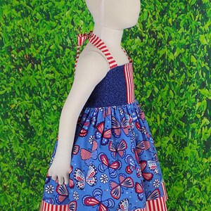 May include: A blue and red sleeveless dress with a butterfly print. The dress has a red and white striped trim at the bottom.