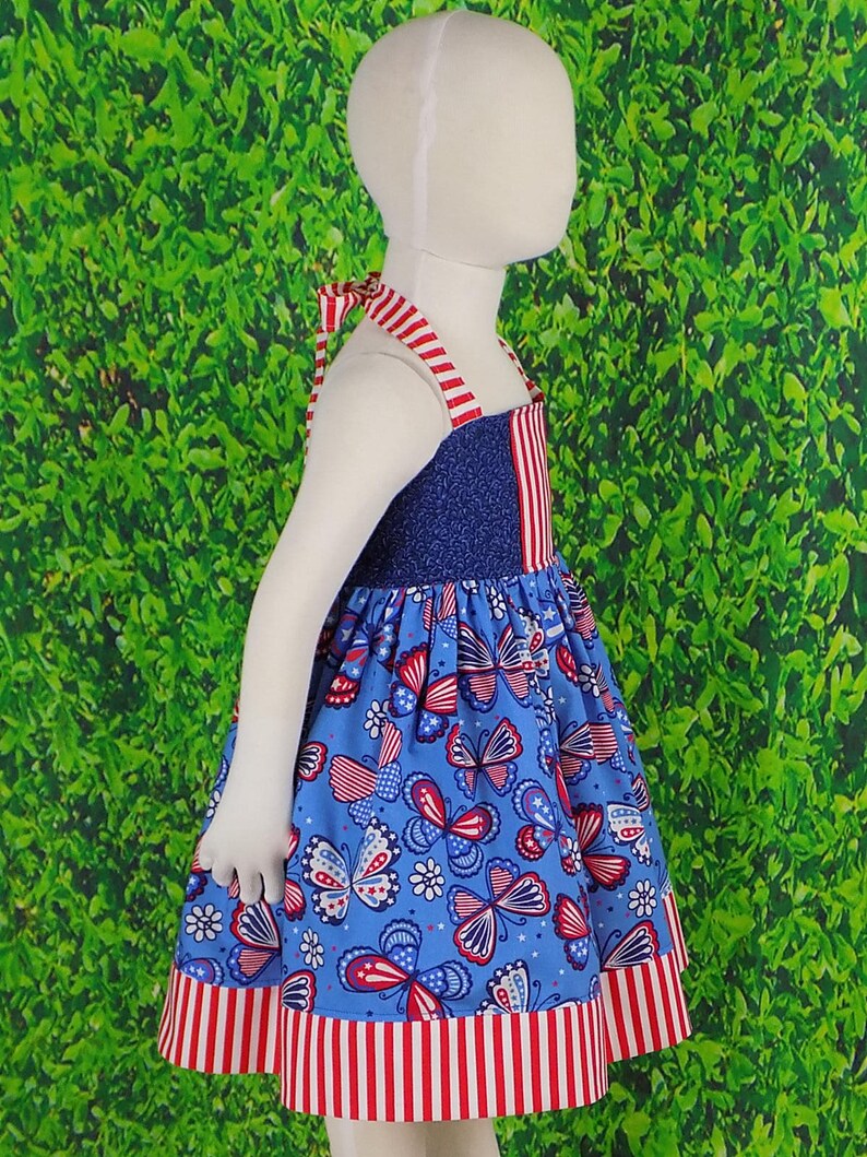 May include: A blue and red sleeveless dress with a butterfly print. The dress has a red and white striped trim at the bottom.