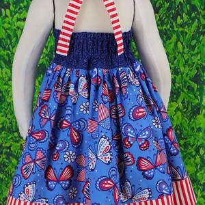 May include: A blue and red sleeveless dress with a halter top and a butterfly print. The dress has a red, white, and blue striped trim.