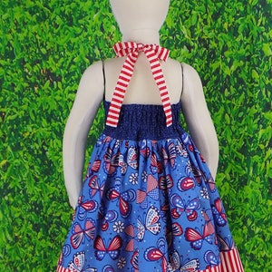 May include: A blue and white dress with a red, white, and blue butterfly print. The dress has a halter neckline and a red and white striped trim.