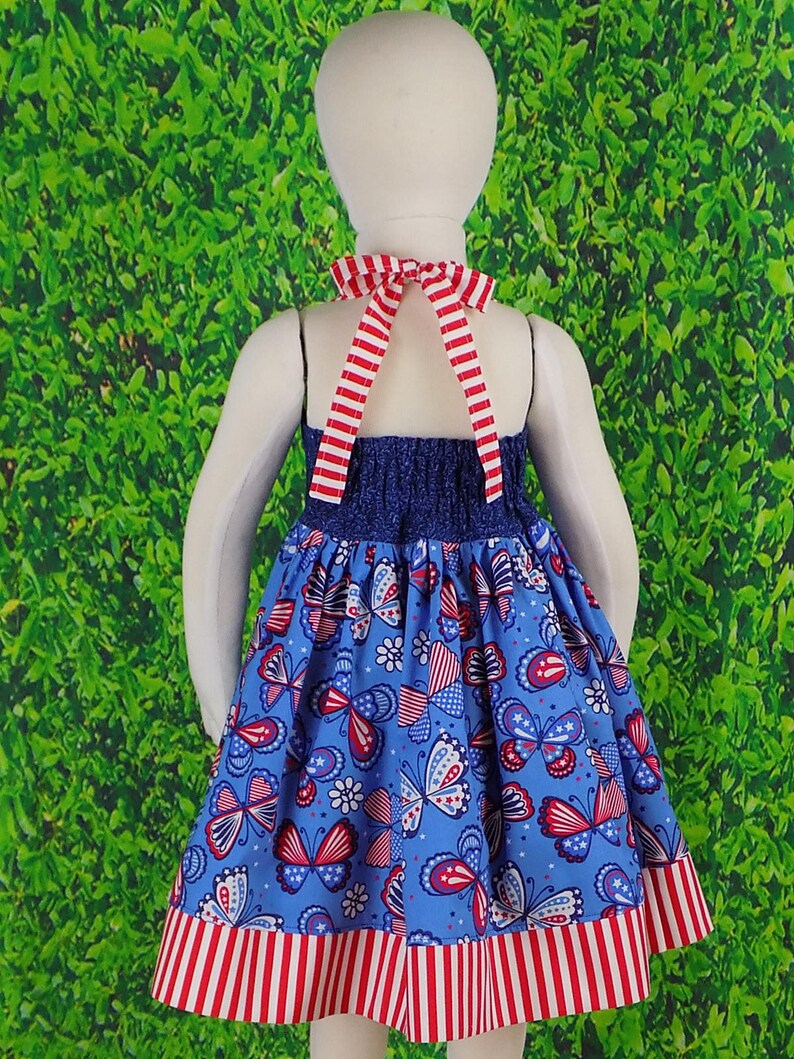 May include: A blue and white dress with a red, white, and blue butterfly print. The dress has a halter neckline and a red and white striped trim.