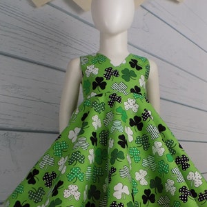 May include: A green sleeveless dress with a shamrock print. The dress has a V-neck and a full skirt. The dress is perfect for St. Patrick's Day.