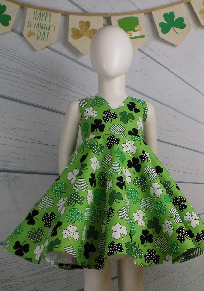 May include: A green sleeveless dress with a shamrock print. The dress has a V-neck and a full skirt. The dress is perfect for St. Patrick's Day.