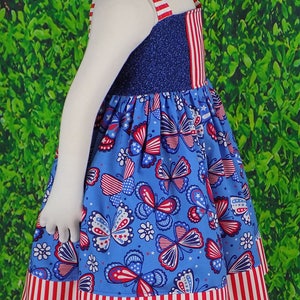 May include: A blue and red sleeveless dress with a butterfly print. The dress has a red and white striped trim around the bottom.