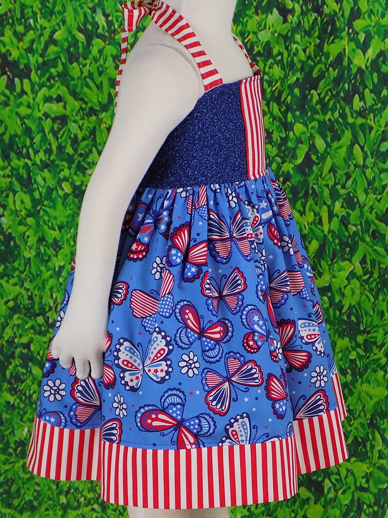May include: A blue and red sleeveless dress with a butterfly print. The dress has a red and white striped trim around the bottom.