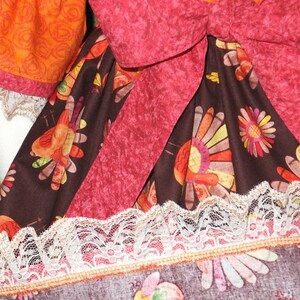 May include: A brown fabric with a pattern of colorful turkeys and flowers. The fabric has a pink ribbon tied around it and a white lace trim.