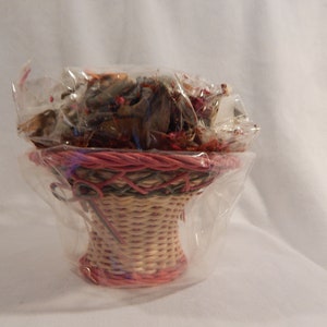 May include: A small wicker basket with a pink and green woven design, filled with dried floral arrangements and wrapped in clear plastic.