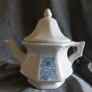 May include: White ceramic teapot with a blue floral design and a lid. The teapot has a rounded body and a spout on the side.