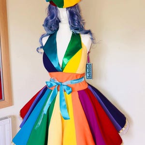 May include: A rainbow-colored dress with a matching hat. The dress has a fitted bodice and a full skirt with a rainbow stripe pattern. The hat is a round, multi-colored beret with a pom-pom on top. The dress is made of a soft, comfortable fabric and is perfect for a fun and festive occasion.