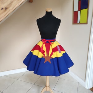 May include: A blue, yellow and red circle skirt with a star and the state of Arizona printed on it. The skirt is on a mannequin and has a red ribbon tied around the waist.